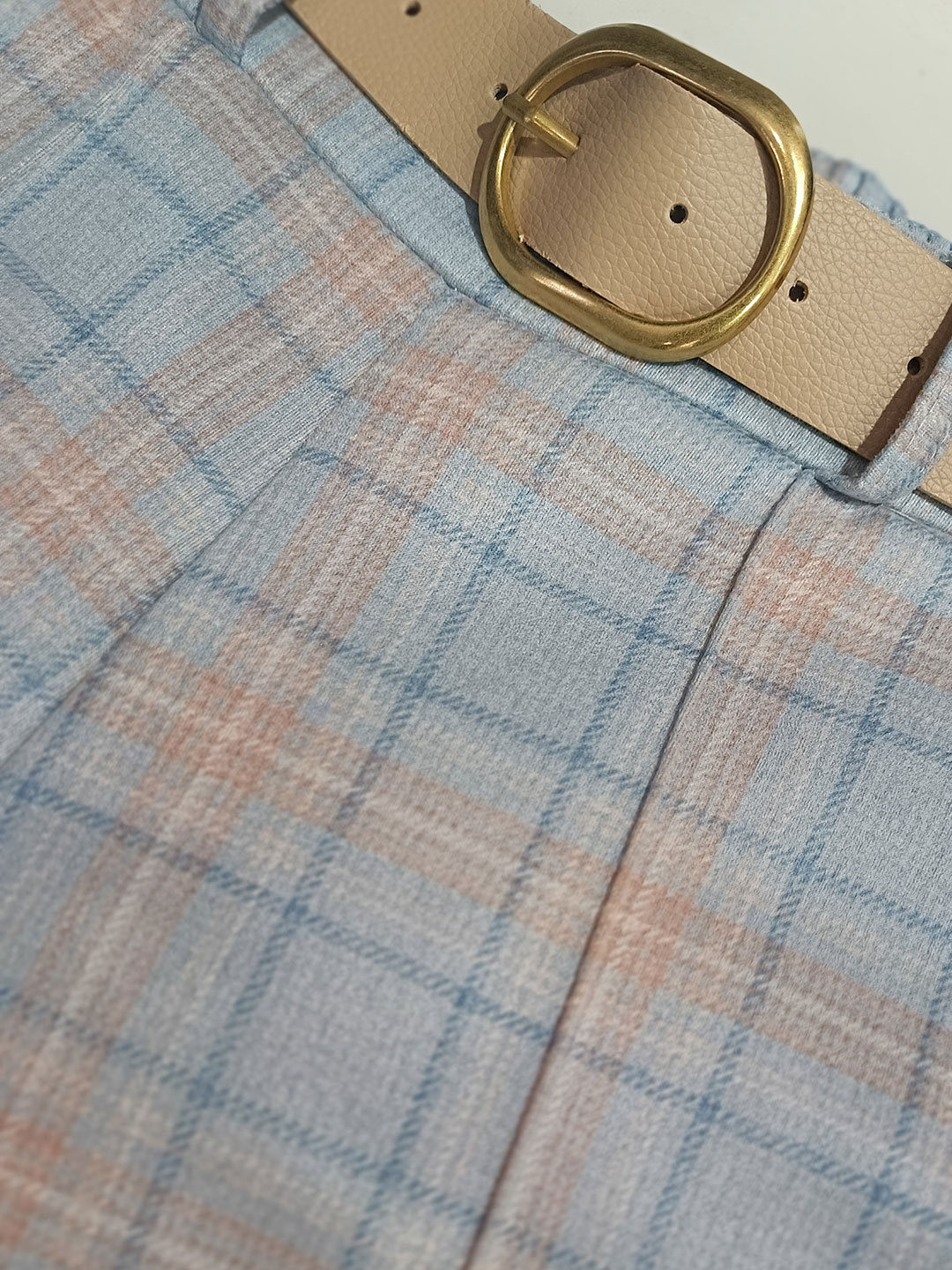 Detalle de la hebilla dorada y tejido del pantalón de cuadros azul y rosa.