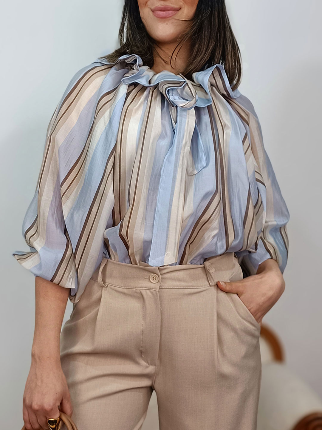 blusa de rayas azul con lazada al cuello y mangas abullonadas combinada con pantalón beige