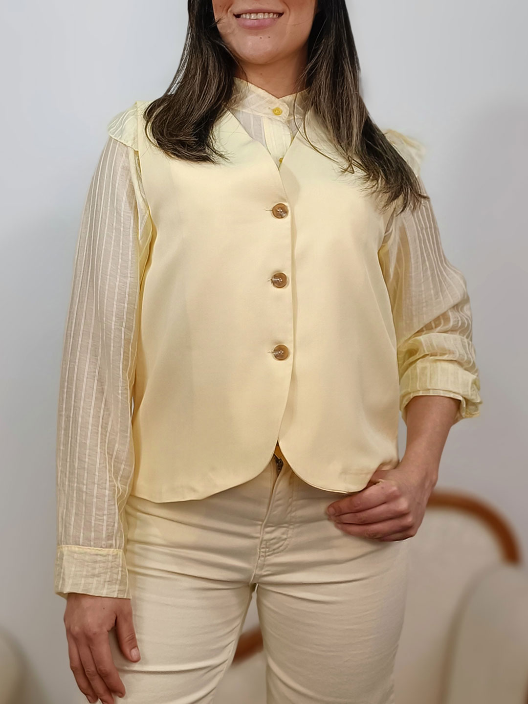 chaleco sastre amarillo vainilla con botones marrones sobre blusa de rayas.